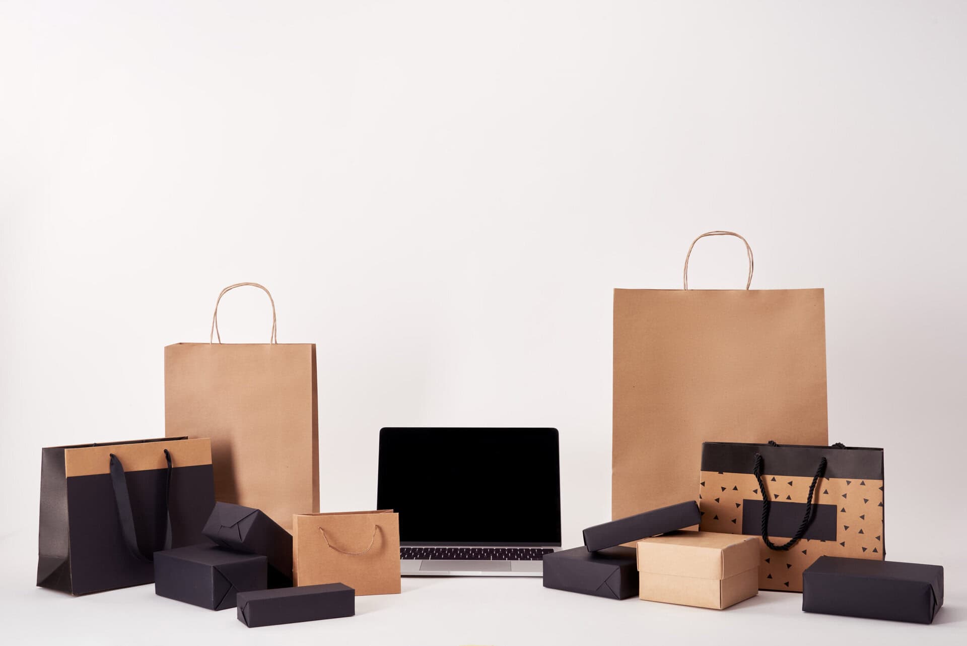 laptop with blank screen with shopping bags and boxes on white surface, black friday concept
